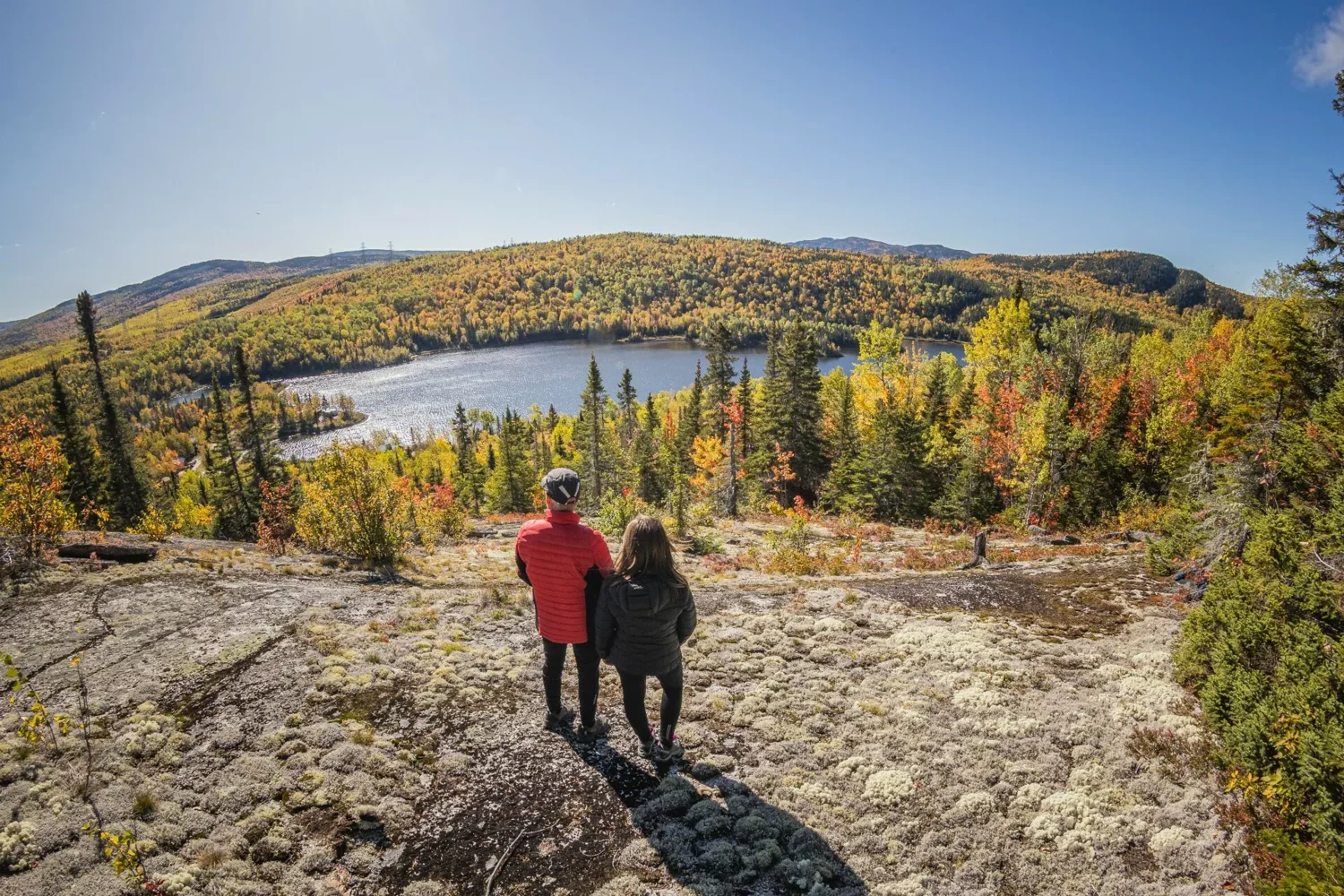 A couple looking at a lake ringed by autumn-coloured hills in Charlevoix